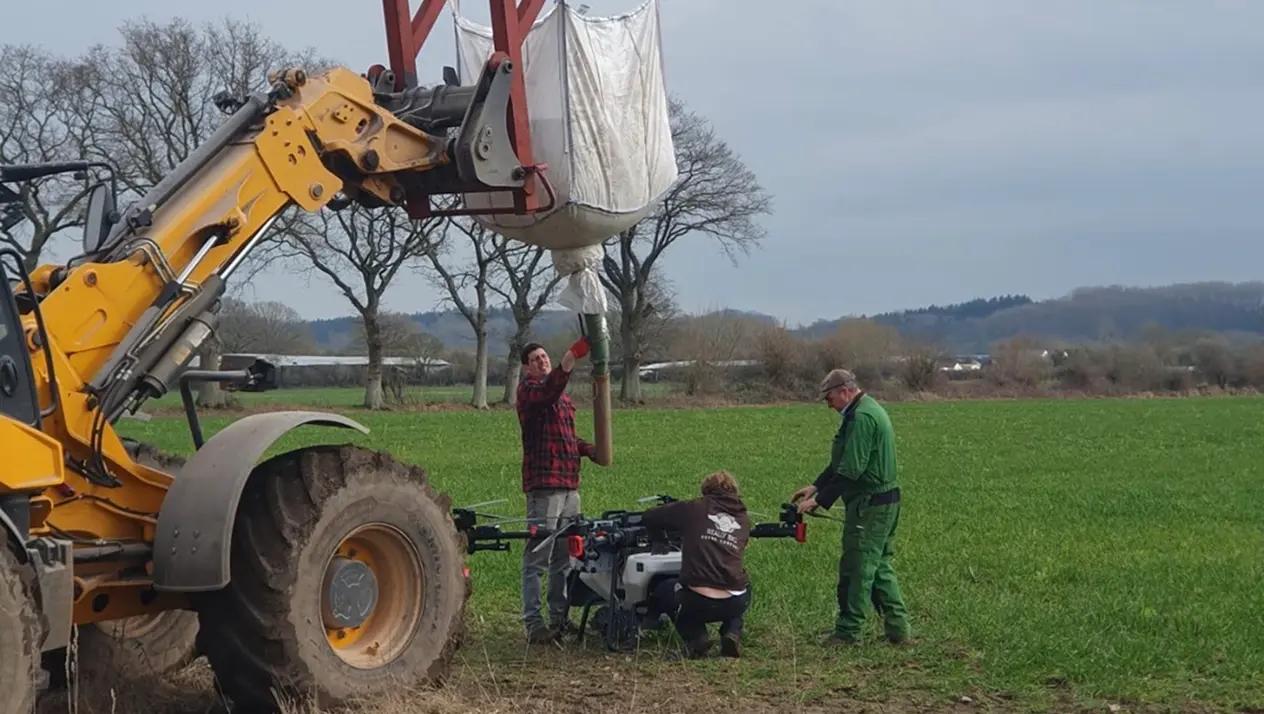 Loading the drone hopper with seed via JCB ahead of a cover crop spreading operation