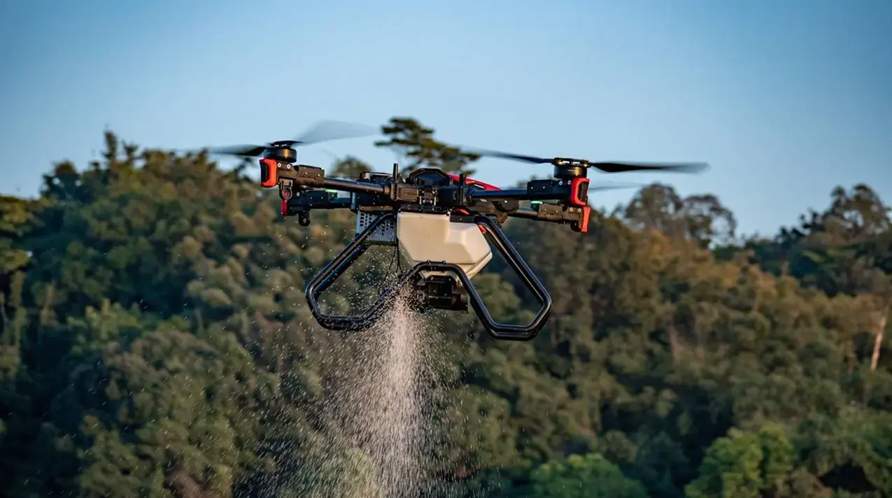 XAG P100 Pro drone broadcasting cover crop seed over an arable field from above