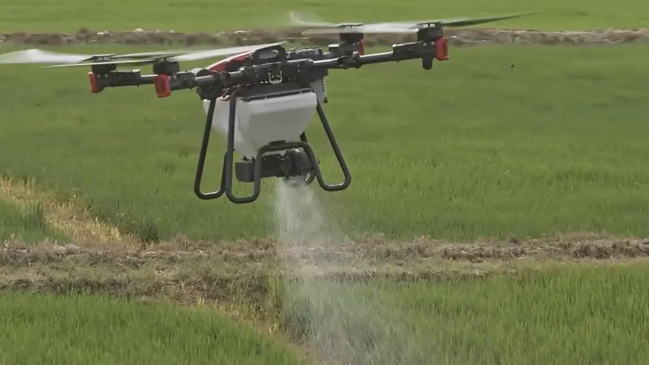 Agricultural drone spreading granular fertiliser at close range over a UK arable field.